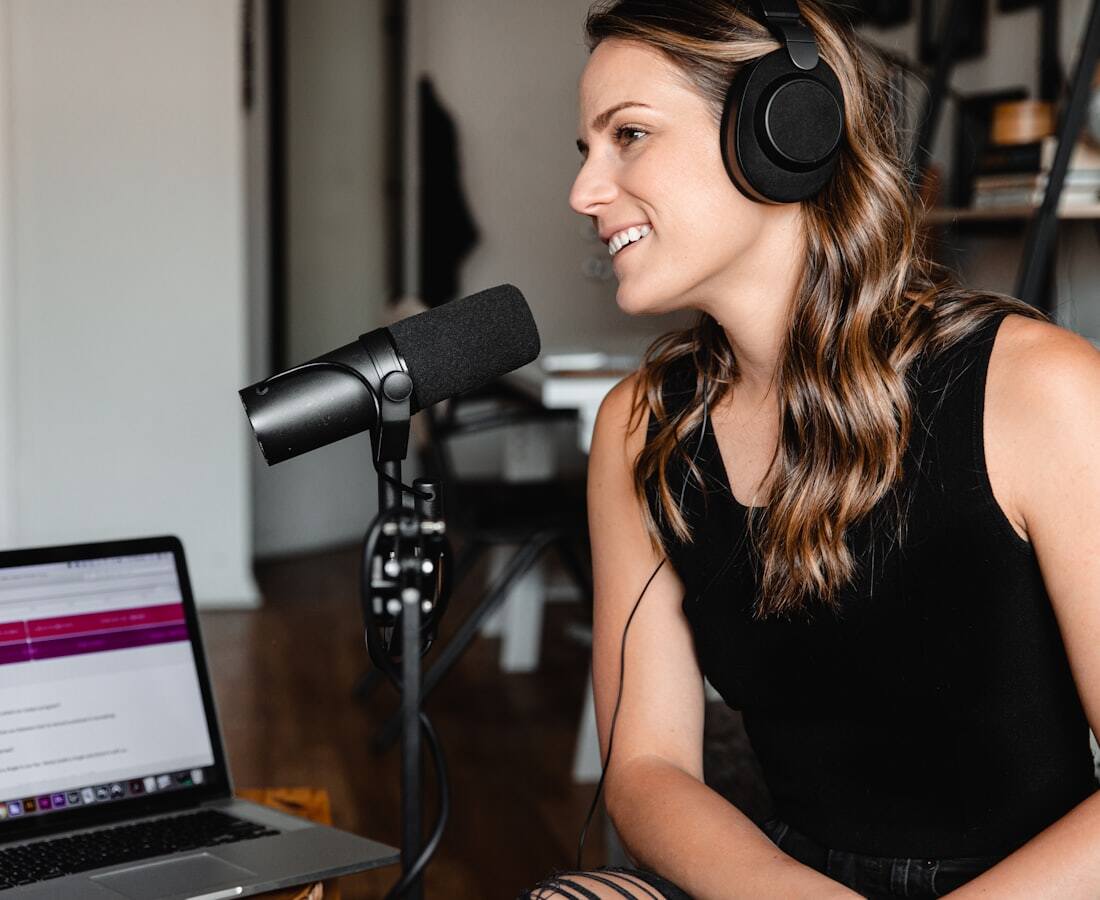 A podcaster wearing headphones, smiling as she speaks into a studio microphone